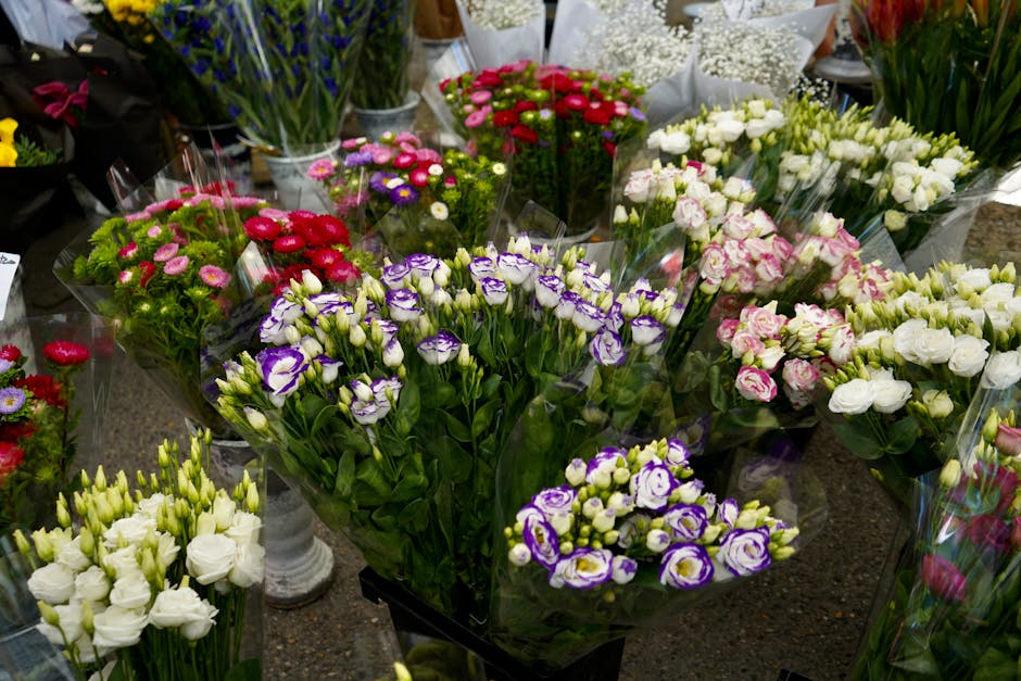 A vibrant display of freshly cut flowers arranged in bouquets on a florist's table, featuring purple and white lisianthus, pink and white roses, small pink and red daisies, and sprigs of white baby's 