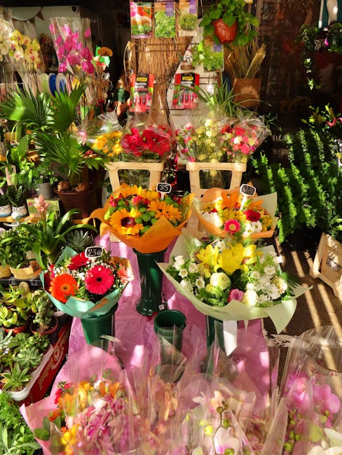 A vibrant display of fresh flower bouquets arranged on a pink table at a florist shop, featuring a variety of colorful blossoms including yellow, pink, red, and white flowers, wrapped in decorative pa